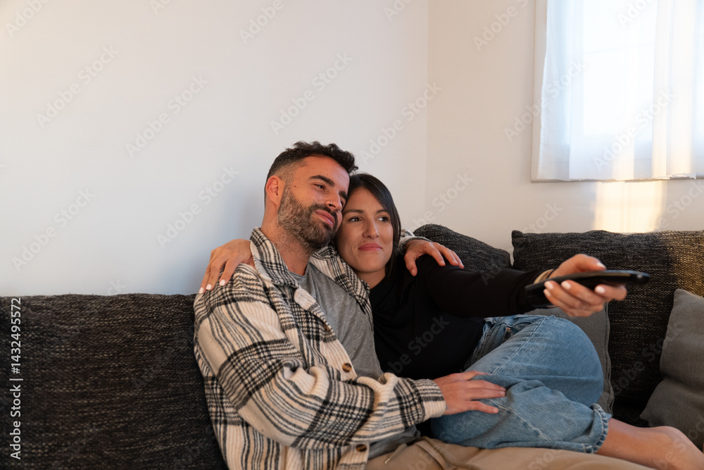 Obraz premium Couple cuddling, watching tv while relaxing together on living room sofa, sharing intimate moment at home