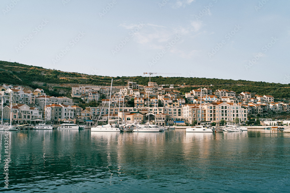 Obraz premium Sailing yachts are moored off the coast of a bay with colorful houses. Lustica, Montenegro