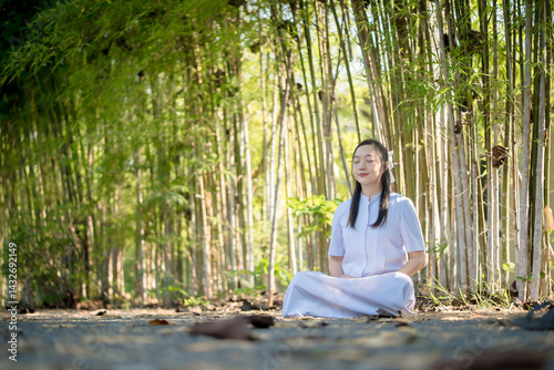 Young Asian woman peacefully meditating in a serene bamboo forest, eyes closed, embracing mindfulness and spiritual calmness in natural surroundings photo