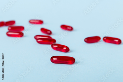 Heap of red pills on colored background. Tablets scattered on a table. Pile of red soft gelatin capsule. Vitamins and dietary supplements concept