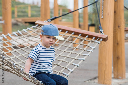 Lifestyle. A cute little boy is sitting in a hammock on a modern outdoor playground. The concept of family entertainment and leisure.