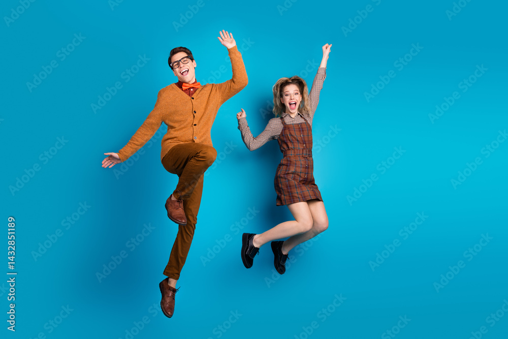 Happy young couple in stylish retro outfits jumping joyfully against a vibrant blue background