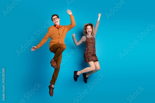 Obraz na płótnie Happy young couple in stylish retro outfits jumping joyfully against a vibrant blue background w salonie