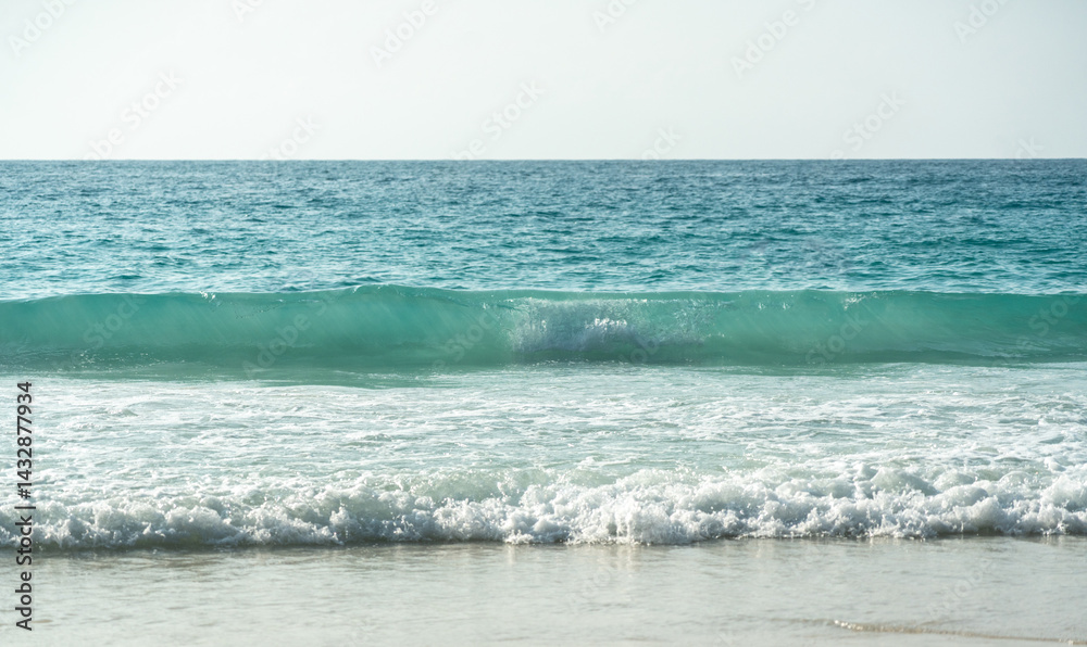 Clear turquoise waves gently crashing on a peaceful sandy beach at a tropical island coastline