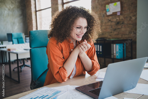 Smiling businesswoman enjoying a moment in a modern office with light-filled windows and casual style, surrounded by documents and a laptop