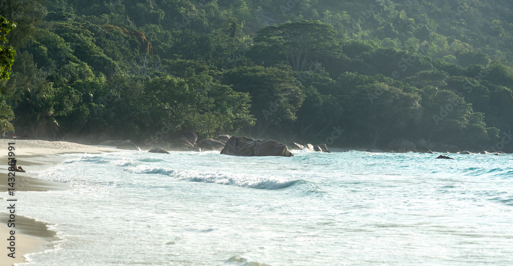 Tropical island beach in Seychelles with jungle, granite boulders, and soft sea waves