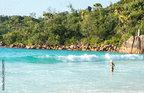 Obraz na płótnie Woman in bikini and hat stands in turquoise sea at a tropical Seychelles beach with granite boulders w salonie