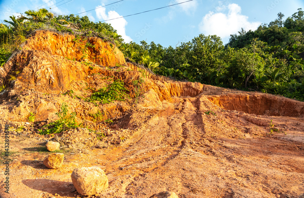 Red tropical soil and rough terrain on a hillside of Seychelles island under bright sunlight