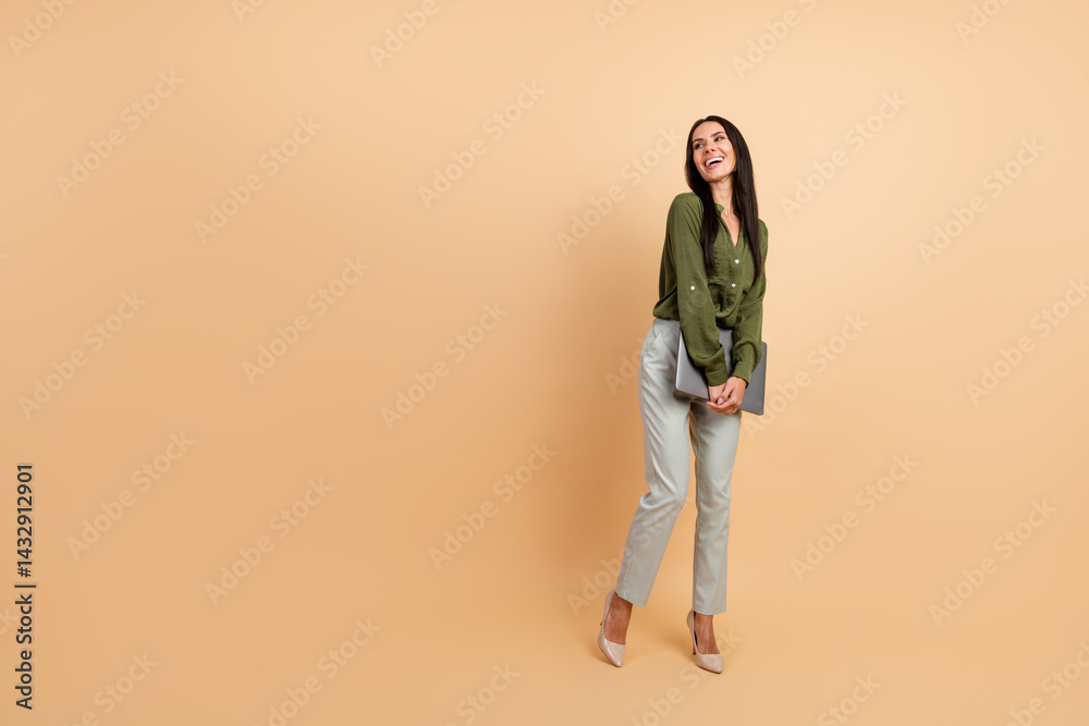 Fototapeta premium Elegant professional woman in green top holding a tablet, posing confidently against a beige background