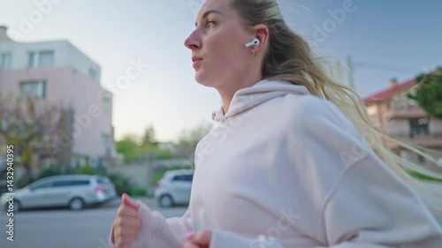 side view portrait of Sporty girl running on a spring city, healthy lifestyle. Young fitness sport woman with earbuds smiling and running slow motion