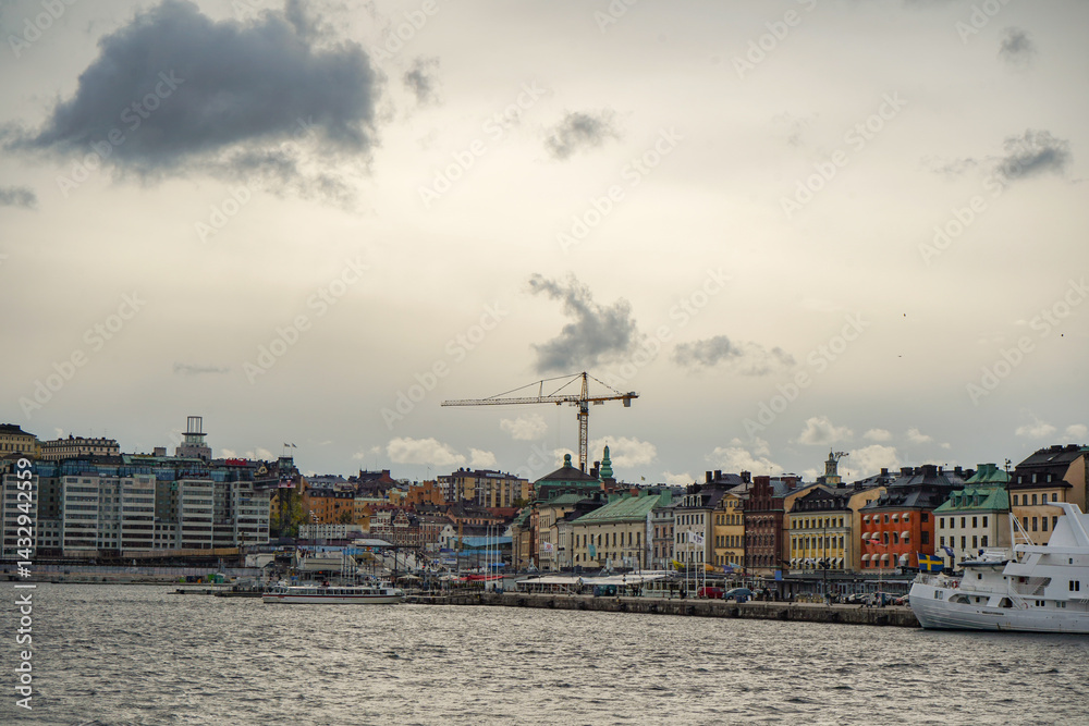 Fototapeta premium Wide angle view of Scandinavian colorful houses next to the seaside with a crane and grey cloudy autumn sky in the background, Stockholm, Sweden