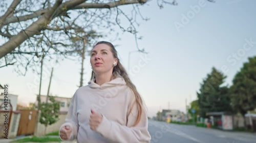 front view portrait of Sporty girl running on a spring city, healthy lifestyle. Young fitness sport woman with earbuds smiling and running slow motion