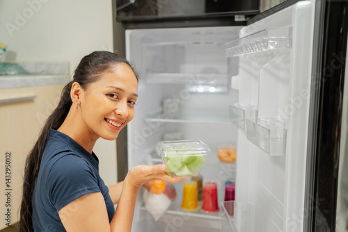 A happy woman lovingly organizes vibrant fresh fruits and vegetables in her fridge