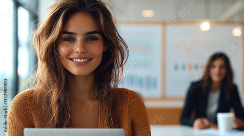 professional woman smiling in modern office environment, showcasing confidence and positivity while working on laptop. background features charts and graphs, indicating business setting
