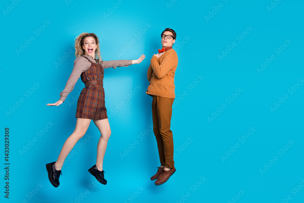 Energetic young couple in retro-style outfits jumping against blue background