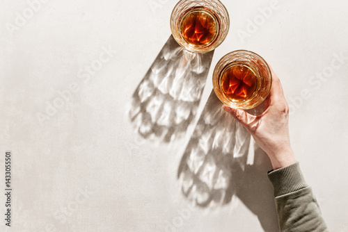 Two Whiskey Glasses with Shadows and sunlight Reflection on beige background, hand holding glass with alcohol, aesthetic top view summer still life, refraction at crystal shine cups, caustics