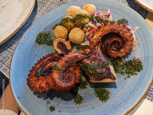 Grilled octopus with potatoes and herb sauce is beautifully presented on a blue plate, ready to serve.
