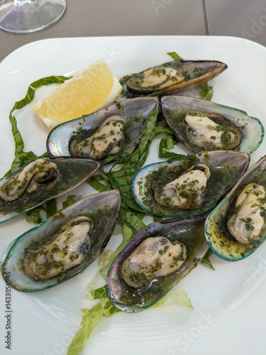 Freshly prepared green mussels, beautifully presented on a white plate with fresh herbs and lemon.