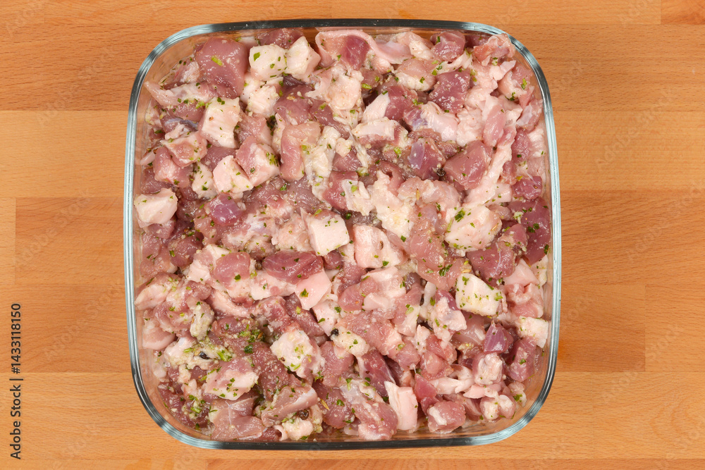 Diced and seasoned pork meat, prepared with spices for sausage making, fills a square glass dish on a wooden surface