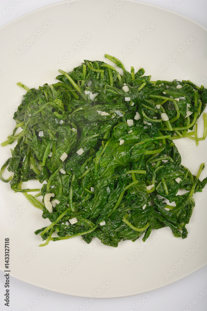 A serving of cooked radish leaves with visible pieces of garlic is presented on a white plate from a top-down perspective