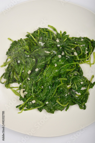 Obraz na płótnie A serving of cooked radish leaves with visible pieces of garlic is presented on a white plate from a top-down perspective w salonie