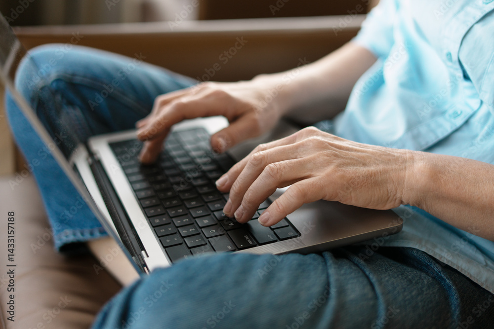 Fototapeta premium Senior woman typing on laptop keyboard while sitting comfortably on sofa