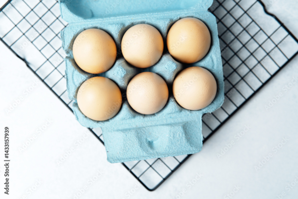 Brown chicken eggs in a blue carton box on light blue background, top view