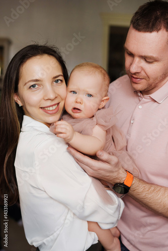 Obraz na płótnie Happy and gentle parents hold baby daughter in pink dress in their arms. w salonie