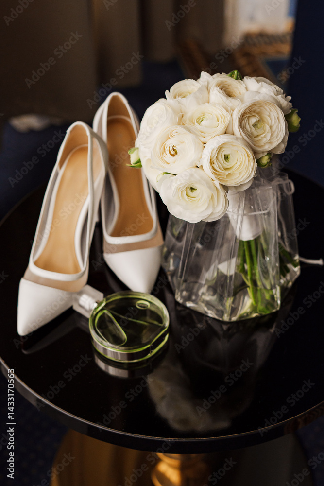 Bridal bouquet, white heeled shoes and a bottle of perfume on a black table.