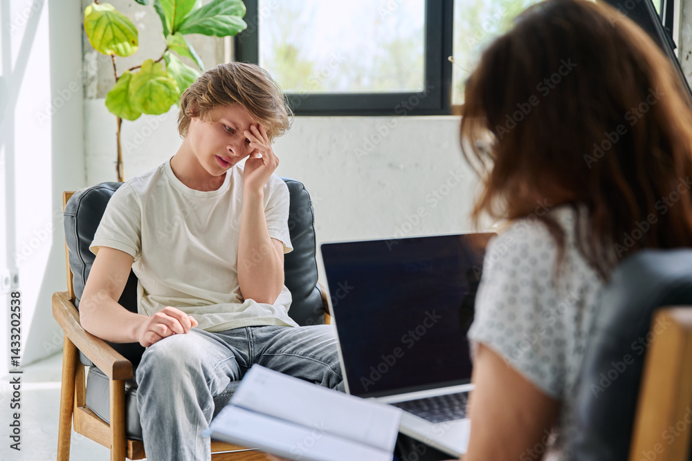 Sad teenage boy in mental therapy session, talking with behavioral psychologist