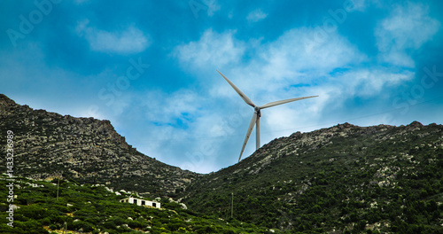 A large wind turbine stands between two green mountains under a blue sky, symbolizing renewable energy in the heart of the Moroccan landscape.