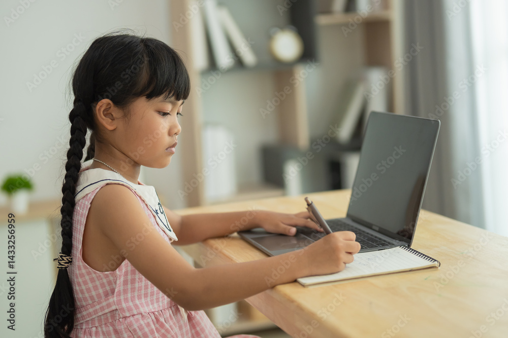 Young girl engaged in studying and writing on notebook with laptop in modern home interior, showcasing focus and educational environment for children Young girl engaged in studying and writing on notebook with laptop in modern home interior, showcasing focus and educational environment for children
