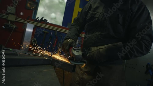 Male welder handling portable professional angle grinder to grind metal in a workshop, medium close up shot. Labor, work, and manufacturing concepts.