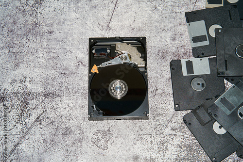 An open 3.5 inch hard disk drive alongside multiple floppy disks on a gray surface.