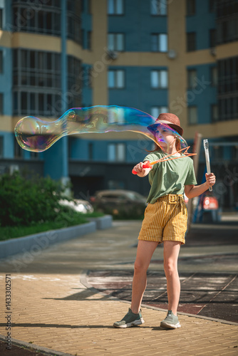 Foto Cute school-age girl blows big soap bubbles in the courtyard of a multi-storey b