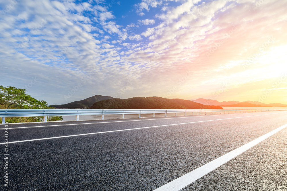 Asphalt road and lake with mountain scenery at sunset
