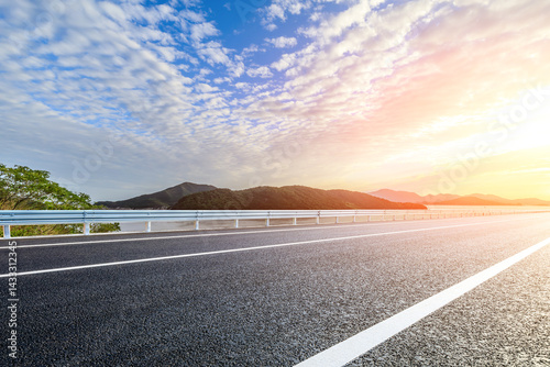 Asphalt road and lake with mountain scenery at sunset