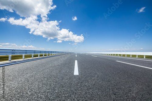 Obraz na płótnie An empty asphalt highway stretches towards the horizon under blue sky w salonie