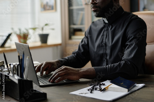 Картината върху платно Medium shot of African American pastor typing on laptops keyboard while sitting