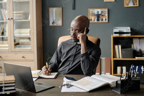 Photos African American pastor leaning his head on hand writing on notebook while prepa