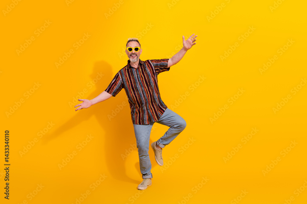 Stylish mature man posing joyfully in colorful outfit against vibrant yellow background Stylish mature man posing joyfully in colorful outfit against vibrant yellow background