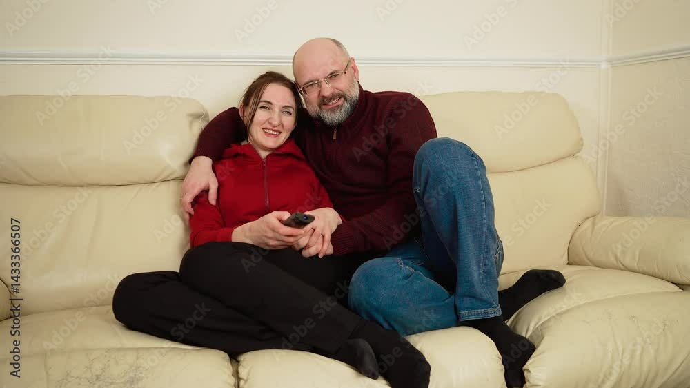 Man and woman sitting on couch in living room, watching television, discussing TV shows and relaxing together. Beautiful family days, cherishing presence, couple valuing small moments. Husband and
