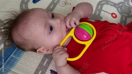 Four-month-old baby girl playfully plays with a rattle