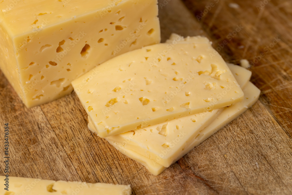cheese with holes for cooking, pieces of sliced cheese on a cutting board, closeup