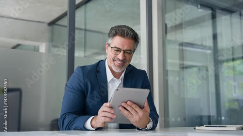 Positive senior businessman entrepreneur sitting at desk working on financial sales project, looking smiling at screen. Mature 50s Latin business man ceo manager using tablet pad computer in office
