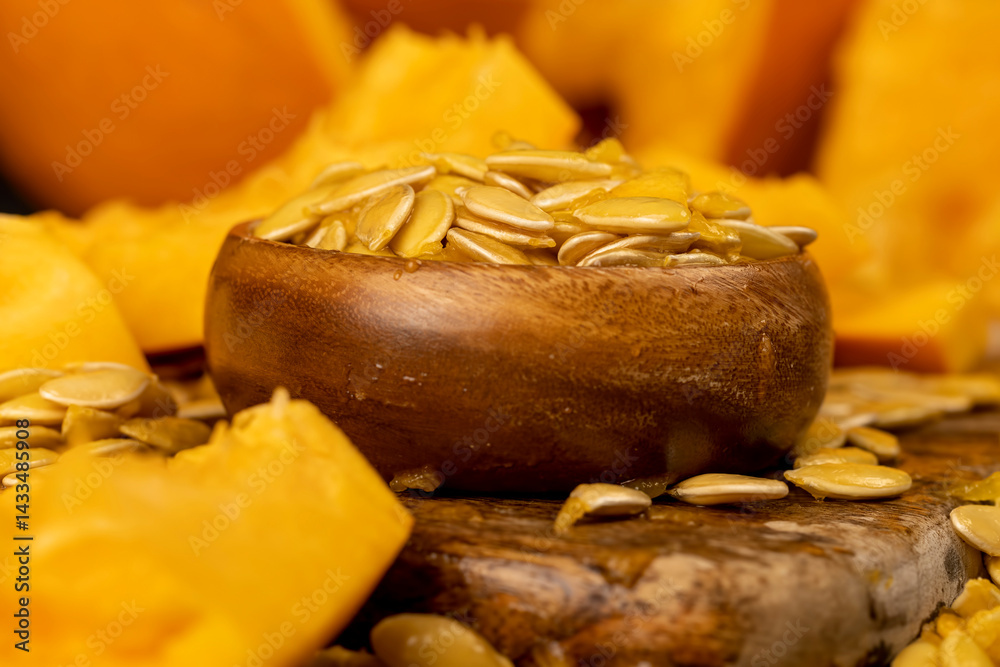 seeds of ripe orange pumpkin, large pumpkin seeds that have just been removed from a cut pumpkin, seeds in a wooden bowl, side view