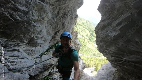 A climber ascends through a narrow vertical gap framed by alpine scenery, part of the exhilarating Hexensteig via ferrata in Switzerland.