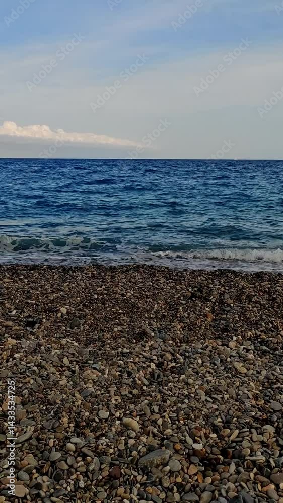 View from the beach in Nice, France. Smooth pebbles in the foreground, calm Mediterranean water, and soft clouds in the summer sky. Ideal for travel, relaxation, and nature themes. View from the beach in Nice, France. Smooth pebbles in the foreground, calm Mediterranean water, and soft clouds in the summer sky. Ideal for travel, relaxation, and nature themes.