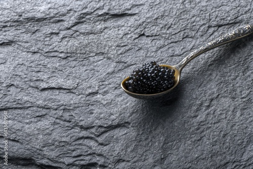 A spoonful of black caviar rests on a dark gray slate surface.  The elegant setting highlights the delicacy's luxurious quality.