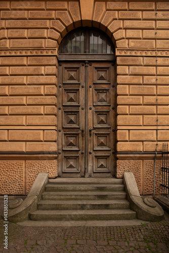 Elegant antique wooden door with symmetrical decorative elements in medieval town with small staircase against orange brown wall
